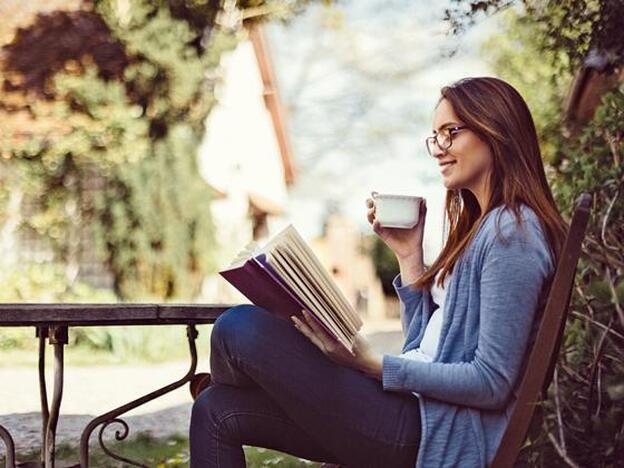 Chica leyendo en el parque tomando café./getty
