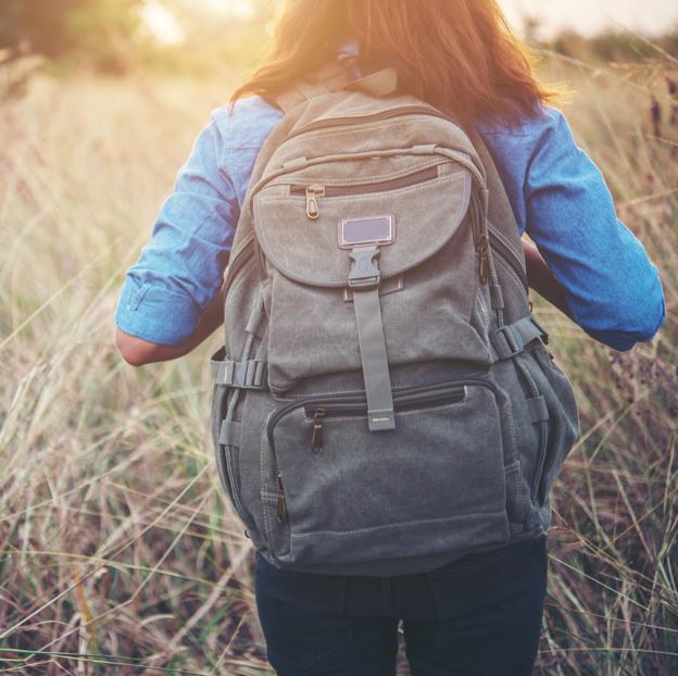 Mujer caminando por el campo con una mochila a la espalda.
