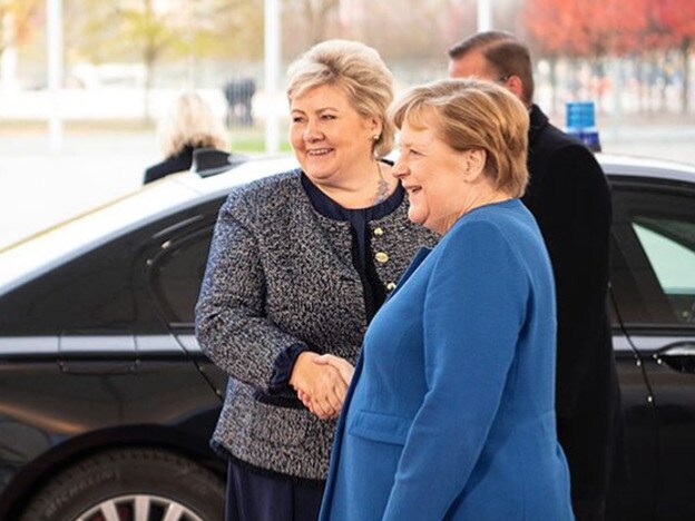Las primeras ministras de Noruega y Alemania, Erna Solberg y Angela Merkel, se estrechan la mano enuna cumbre internacional.
