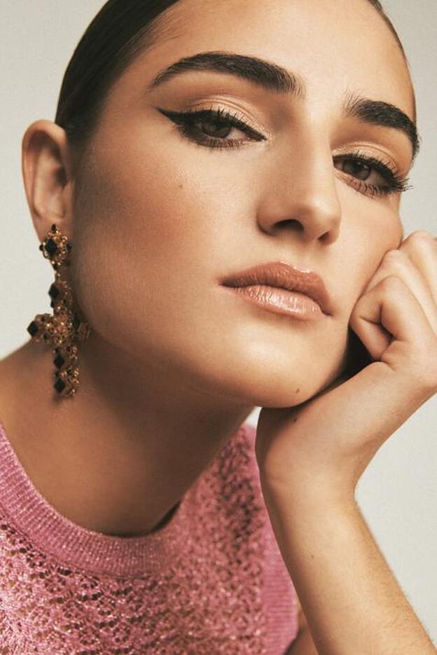 Jersey rosa en encaje de punto lurex y pendientes, de Dolce&Gabbana. En los ojos, línea definida, con acabado en punta ascendente con un toque retro a base de eyeliner líquido Royal Kajal, de la colección de Navidad de Dolce&Gabbana Beauty.