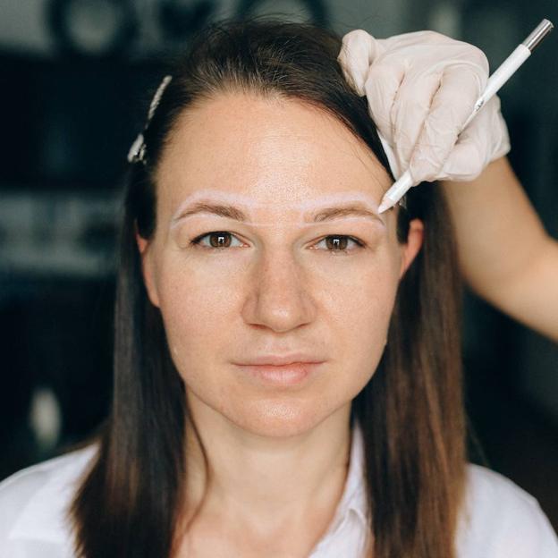 Profesional pintando forma de cejas con lápiz para la depilación