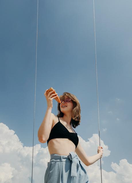 Mujer comiendo un trozo de pizza/PEXELS