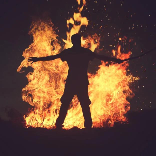 Hombre frente a una hoguera encendida en la playa. 