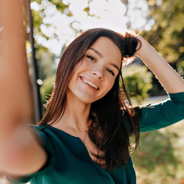 Mujer con blusa verde sonriendo en mitad de la naturaleza. 