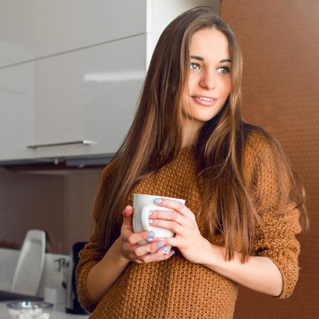 Mujer apoyada en la pared con una taza de café. 