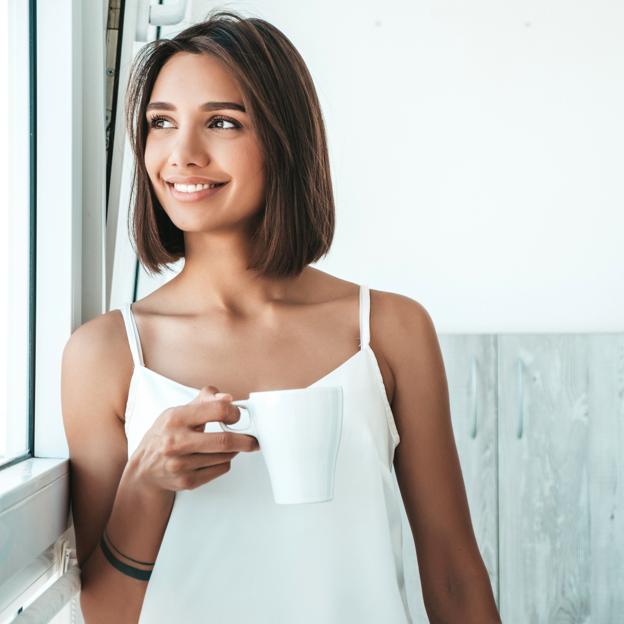 Mujer tomando una taza de infusión frente a la ventana. 