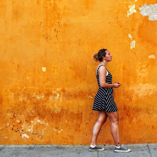 Mujer andando por la acera al lado de una pared naranja. 