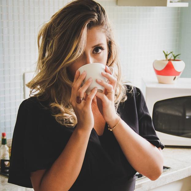 Mujer tomando una taza de infusión apoyada en la encimera de la cocina. 