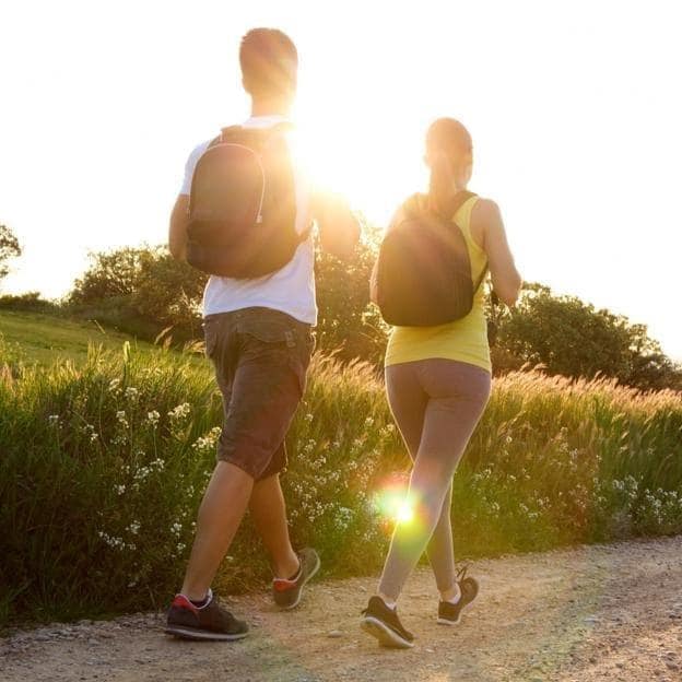 Pareja paseando por el campo con una mochila a la espalda.